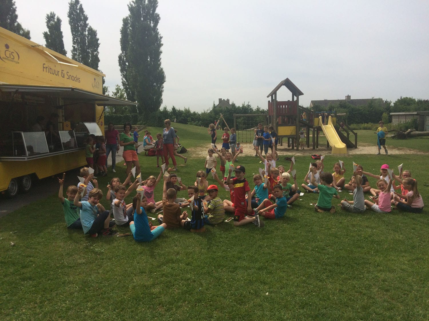 Een geel eetkraam van Cis Events Catering opgebouwd in het gras naast een speeltuin, met een grote groep kinderen