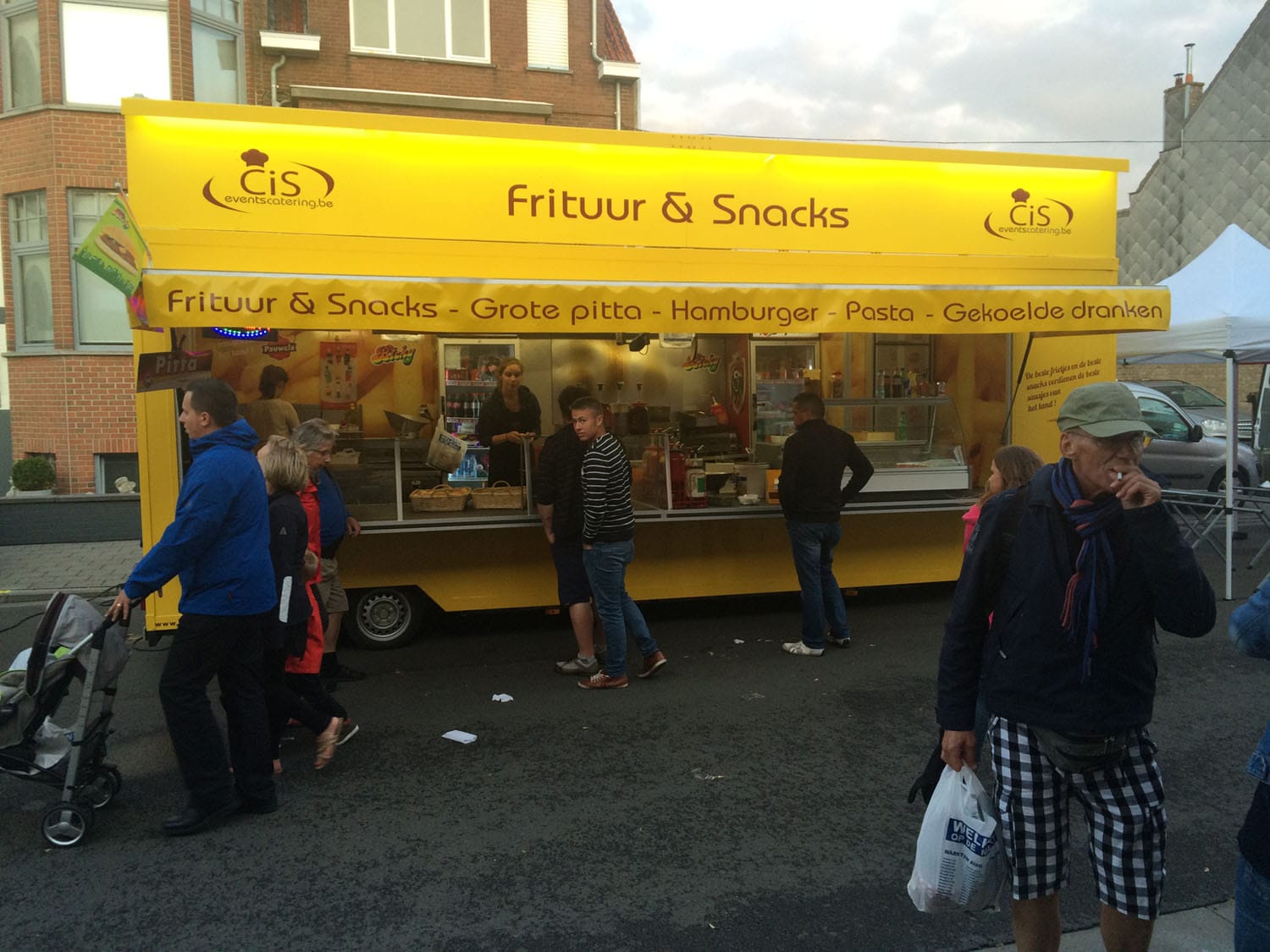 Het gele frietkraam Frituur & Snacks van Cis Events Catering met gasten aan het loket