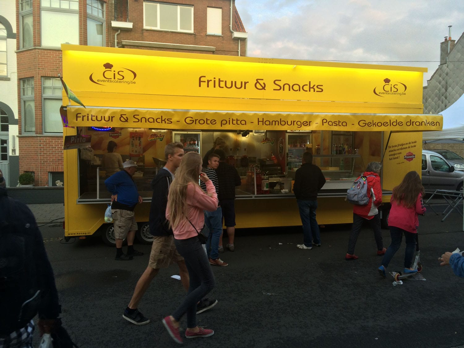Het gele frietkraam van Cis Events Catering met gasten aan het loket op een avondevenement
