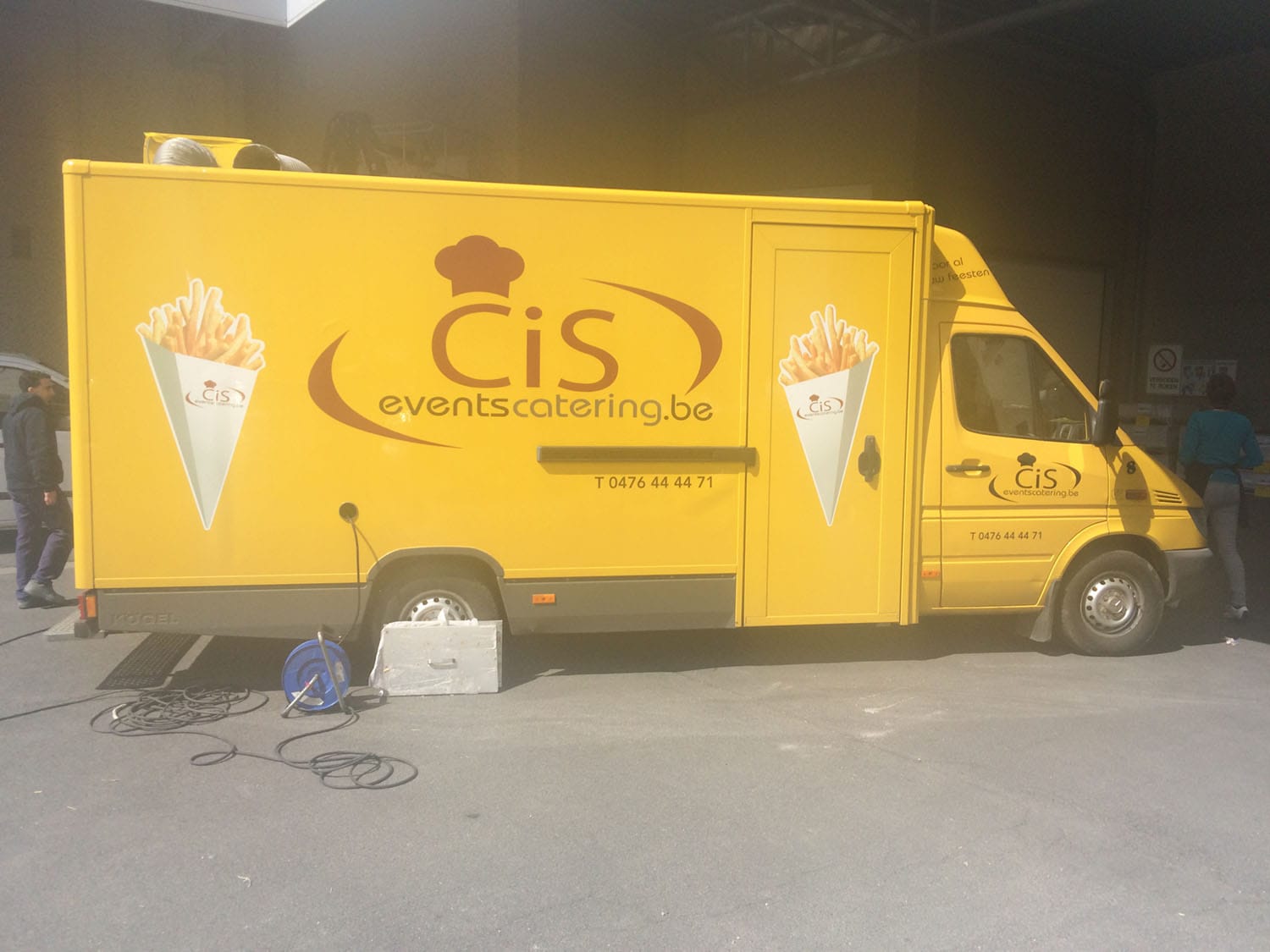 De gele bestelwagen van Cis Events Catering met frietzak-belettering, klaar om uit te rijden