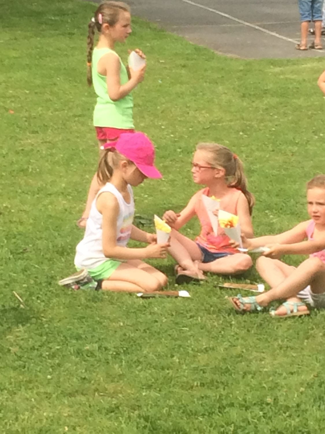 Kinderen zitten in het gras met een frietpuntzak in de hand op een zonnige feestdag